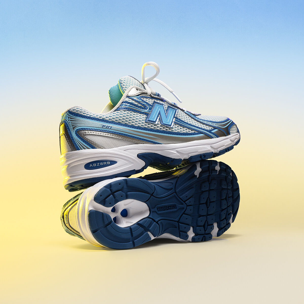 A pair of white and blue 740 shoes stacked on top of each other sitting on a blue and yellow background.